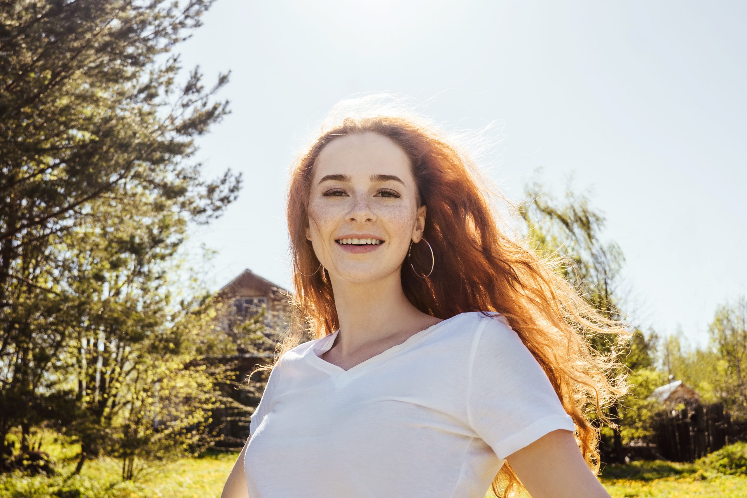 Young happy girl with long curly hair in sunshine. Sky background.